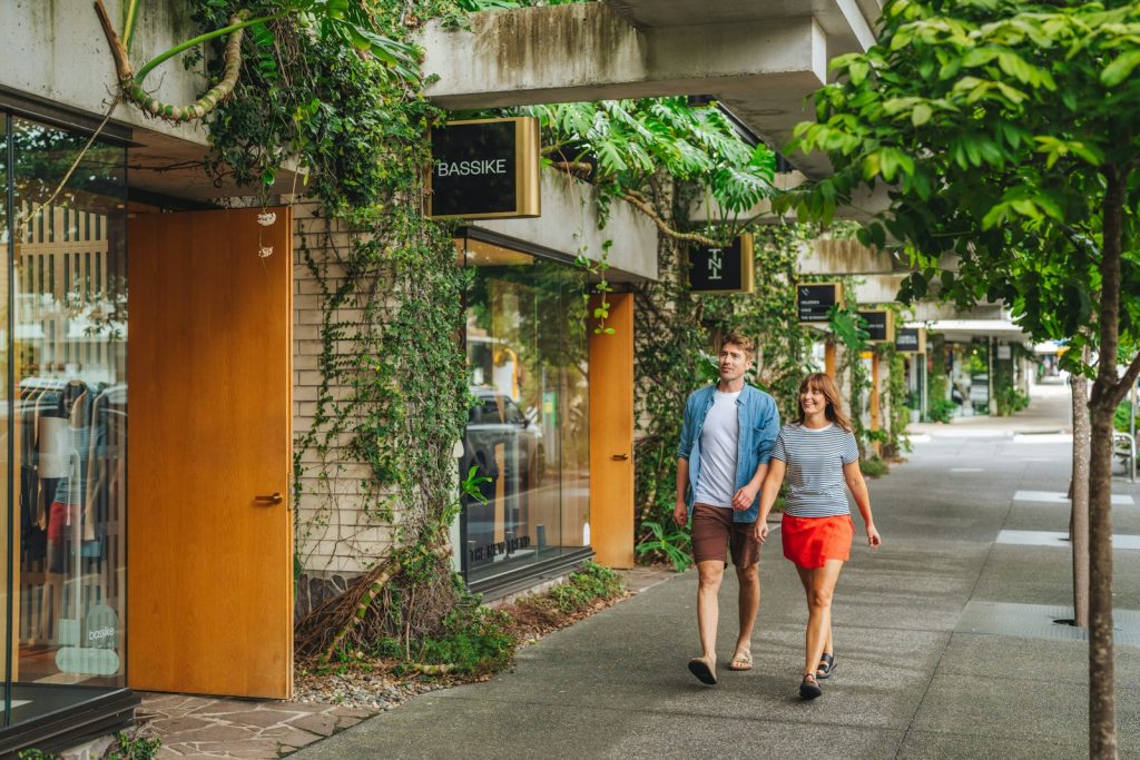 A man and a woman walking past ivy-covered storefronts on a concrete sidewalk